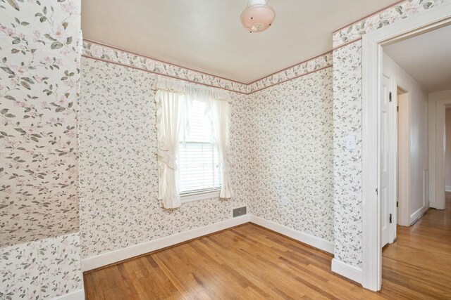 spare room with wood finished floors, wallpapered walls, and baseboards