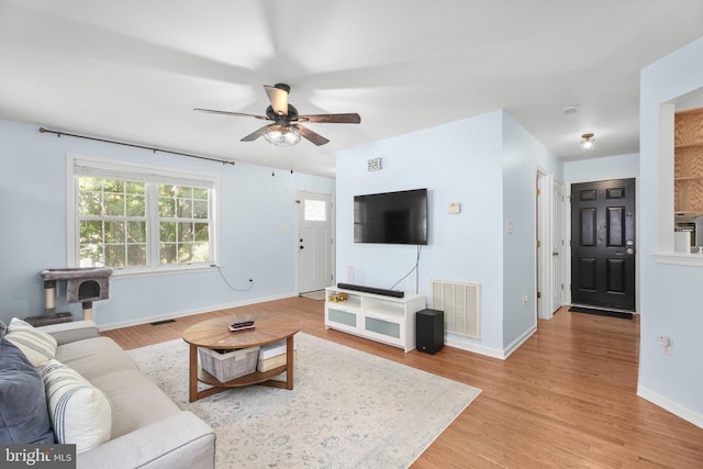 living area featuring baseboards, a ceiling fan, light wood-style flooring, and visible vents