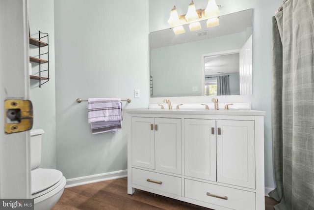 full bathroom featuring a sink, double vanity, toilet, baseboards, and wood finished floors