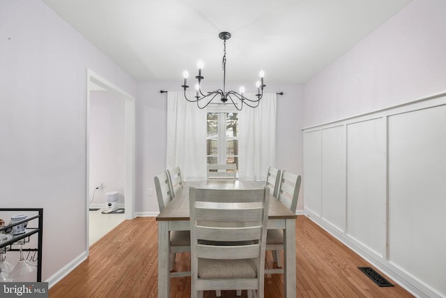 dining area with baseboards, visible vents, light wood finished floors, and a chandelier