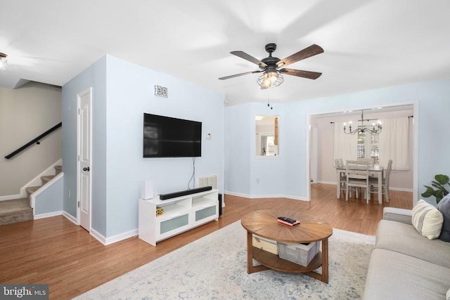 living area with stairway, baseboards, ceiling fan with notable chandelier, and wood finished floors