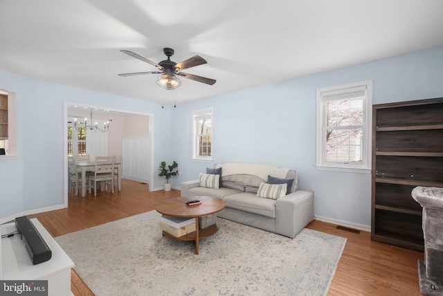 living room featuring plenty of natural light, ceiling fan with notable chandelier, wood finished floors, and visible vents