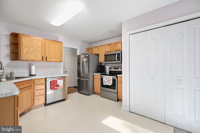 kitchen featuring appliances with stainless steel finishes, open shelves, a sink, light countertops, and light floors