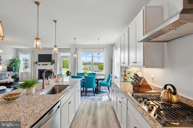 kitchen featuring wall chimney range hood, a sink, stainless steel appliances, and white cabinets