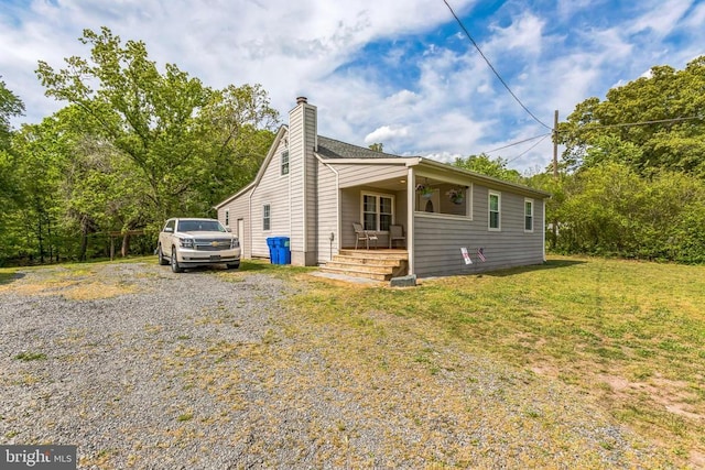 view of front of home featuring a chimney, driveway, covered porch, and a front lawn