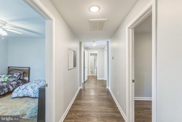 hallway with baseboards, visible vents, and dark wood finished floors
