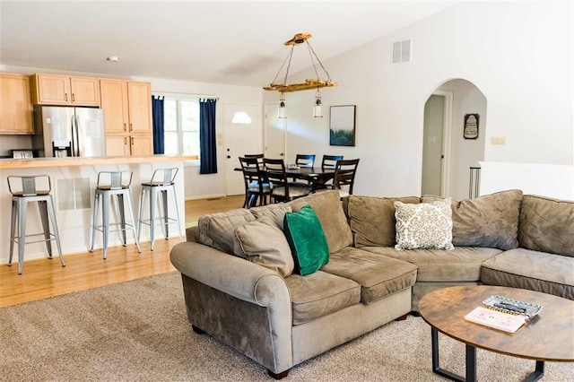 living area featuring lofted ceiling, light wood finished floors, visible vents, arched walkways, and light colored carpet