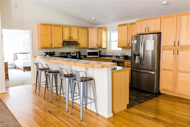 kitchen featuring a peninsula, stainless steel appliances, wood finished floors, under cabinet range hood, and light brown cabinetry