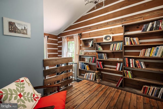 living area featuring hardwood / wood-style flooring, lofted ceiling, wooden walls, and a chandelier