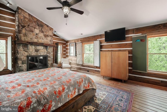 bedroom with wood-type flooring, vaulted ceiling, wooden walls, multiple windows, and a stone fireplace
