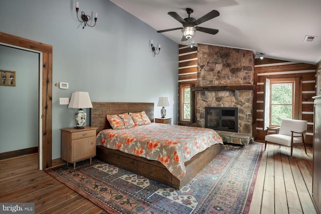 bedroom with vaulted ceiling, hardwood / wood-style floors, a stone fireplace, and a ceiling fan