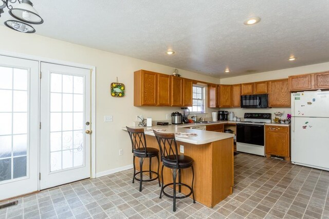 kitchen featuring sink, white appliances, a breakfast bar, a textured ceiling, and kitchen peninsula