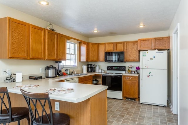 kitchen with sink, a kitchen bar, white appliances, kitchen peninsula, and a textured ceiling