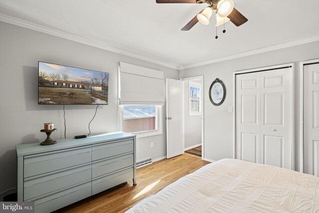 bedroom featuring multiple closets, crown molding, ceiling fan, and light wood-type flooring