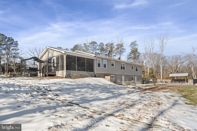 snow covered back of property featuring a sunroom