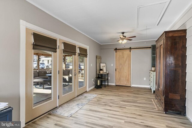 interior space with crown molding, a barn door, ceiling fan, and light hardwood / wood-style flooring