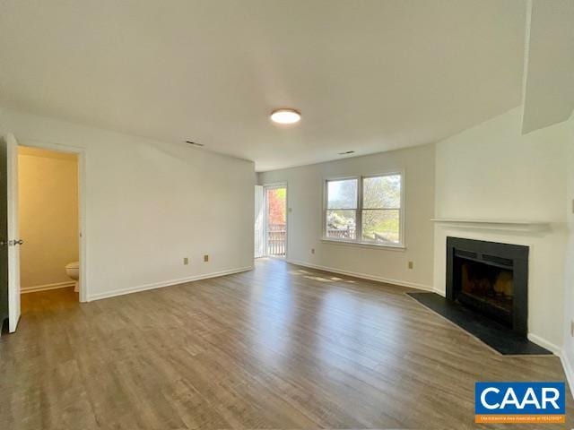 unfurnished living room with wood finished floors, baseboards, and a fireplace with flush hearth