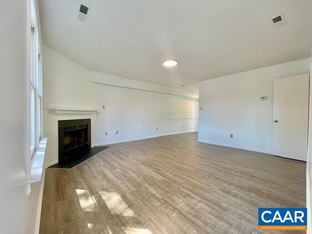 unfurnished living room featuring visible vents, wood finished floors, baseboards, and a fireplace with flush hearth