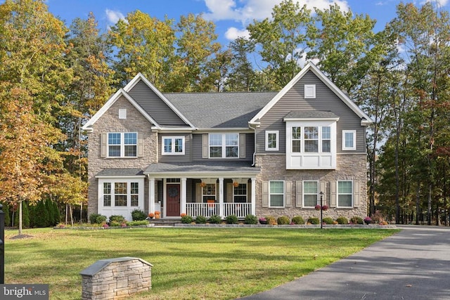 view of front of house featuring covered porch, stone siding, and a front yard