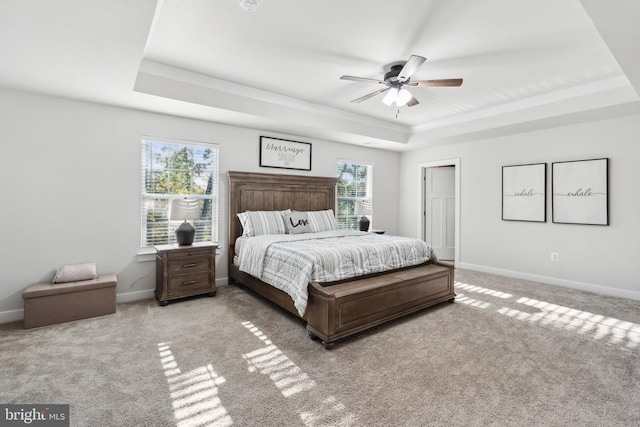 carpeted bedroom featuring a tray ceiling, baseboards, and ceiling fan