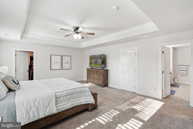 bedroom with a tray ceiling, carpet flooring, a walk in closet, ensuite bath, and baseboards