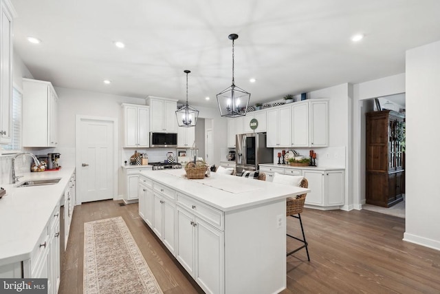 kitchen with a sink, stainless steel appliances, a center island, white cabinetry, and dark wood-style floors