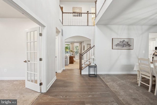 entrance foyer with arched walkways, wood finished floors, stairs, baseboards, and a towering ceiling