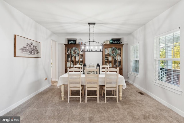 carpeted dining space featuring a chandelier and baseboards