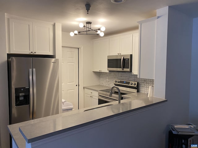 kitchen featuring a peninsula, tasteful backsplash, white cabinetry, a notable chandelier, and appliances with stainless steel finishes