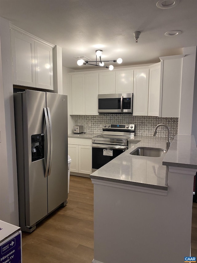 kitchen featuring a peninsula, wood finished floors, a sink, white cabinetry, and appliances with stainless steel finishes