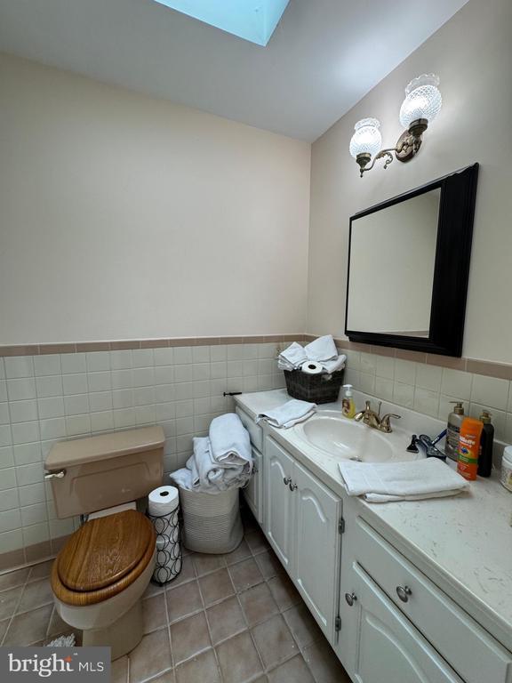 7880 Sir Topas Dr, Warrenton, VA 20186 - half bath with tile walls, vanity, a skylight, toilet, and tile patterned flooring
