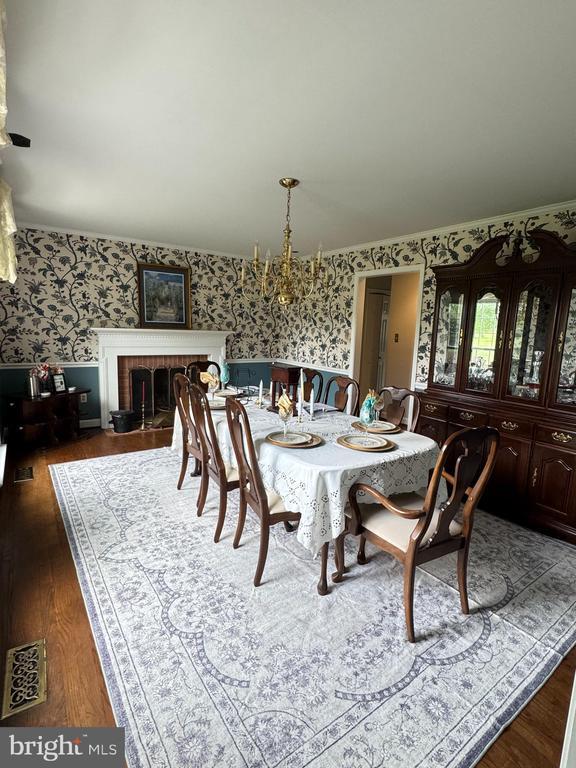 7880 Sir Topas Dr, Warrenton, VA 20186 - dining space featuring wallpapered walls, dark wood-style flooring, a fireplace, a chandelier, and a wainscoted wall