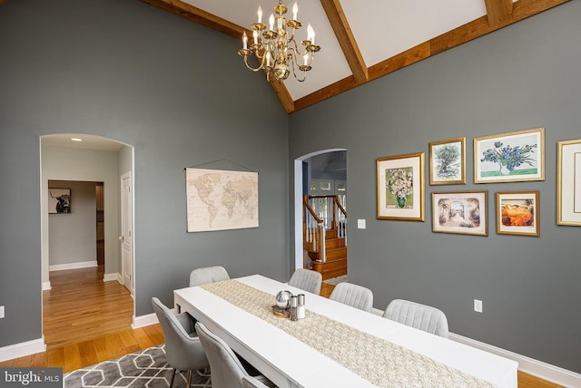 dining area featuring arched walkways, high vaulted ceiling, a chandelier, wood finished floors, and beamed ceiling