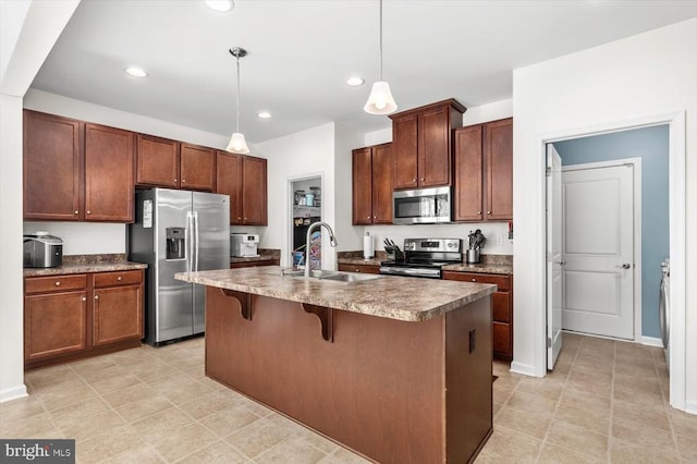 kitchen with a kitchen breakfast bar, decorative light fixtures, appliances with stainless steel finishes, a sink, and an island with sink