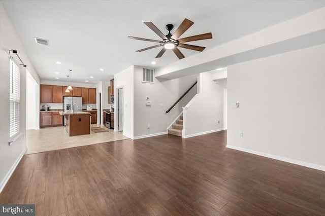 unfurnished living room with visible vents, ceiling fan, wood finished floors, and stairway