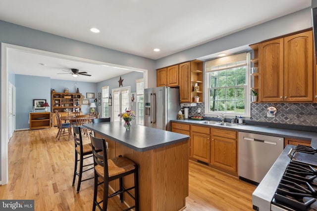 kitchen featuring appliances with stainless steel finishes, open shelves, a sink, dark countertops, and a breakfast bar