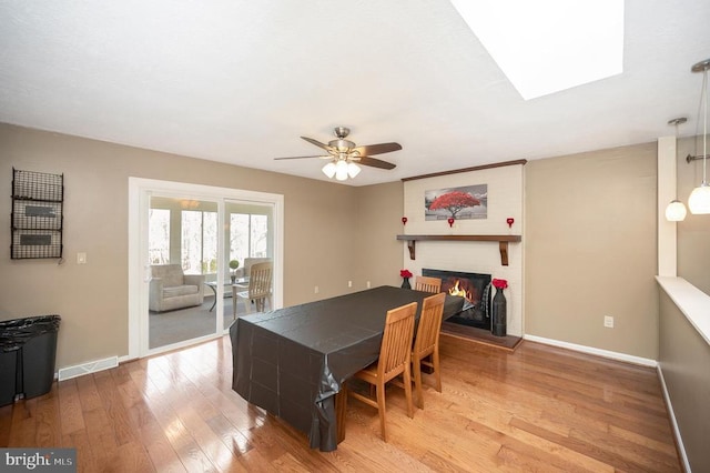 dining area featuring a brick fireplace, wood finished floors, baseboards, ceiling fan, and a skylight