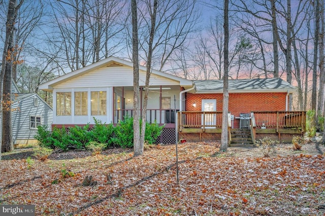 back of house at dusk with brick siding, a wooden deck, a sunroom, and stairs