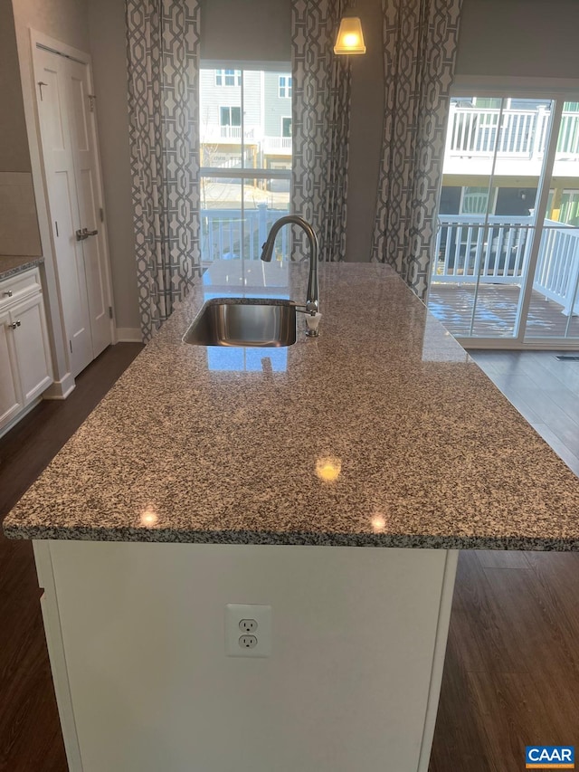 kitchen with dark stone countertops, a sink, white cabinets, a center island with sink, and dark wood-style floors