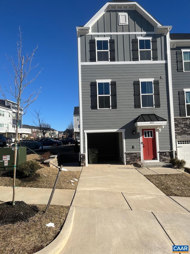 view of front facade featuring an attached garage, board and batten siding, driveway, and stone siding