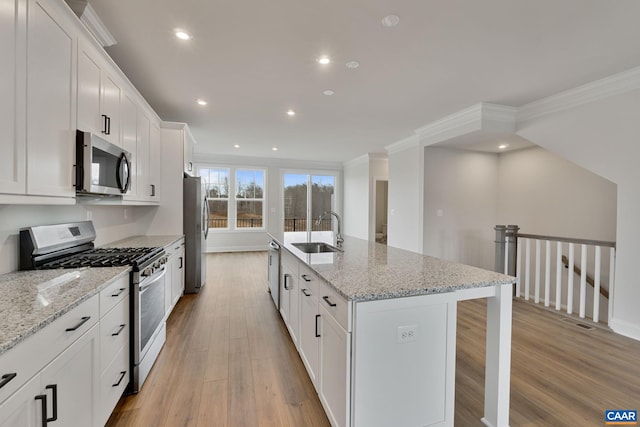 kitchen with appliances with stainless steel finishes, a sink, light wood-style flooring, an island with sink, and white cabinetry