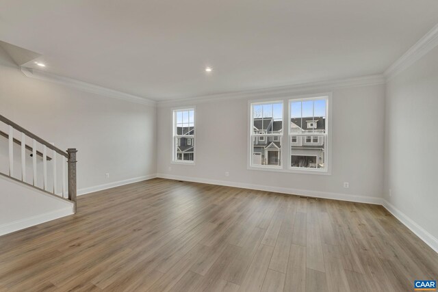 unfurnished living room featuring stairs, ornamental molding, plenty of natural light, wood finished floors, and baseboards