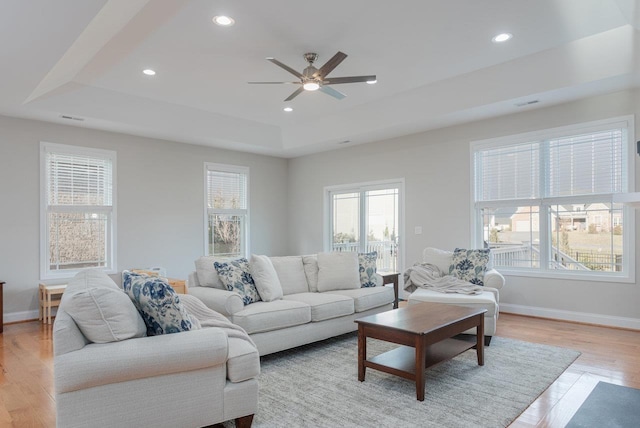 living room featuring ceiling fan, a tray ceiling, and light hardwood / wood-style flooring