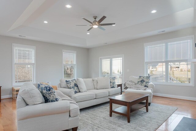 living room featuring ceiling fan, a tray ceiling, and light hardwood / wood-style flooring