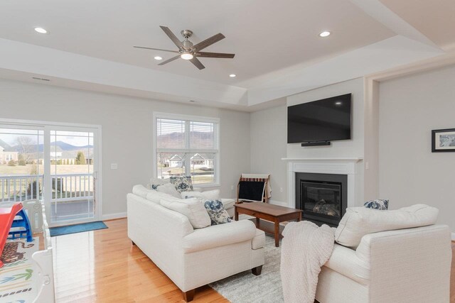 living room featuring ceiling fan, a raised ceiling, a healthy amount of sunlight, and light wood-type flooring