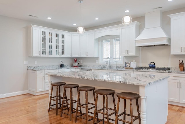 kitchen with stainless steel gas stovetop, a center island, white cabinets, and premium range hood