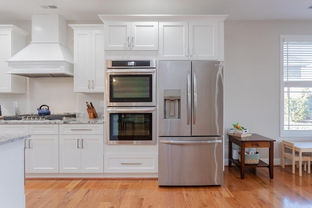 kitchen with stainless steel appliances, premium range hood, plenty of natural light, and white cabinetry