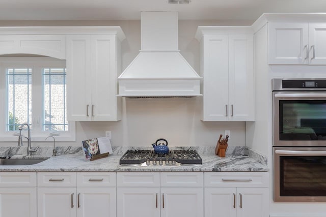 kitchen with premium range hood, white cabinetry, stainless steel appliances, and sink