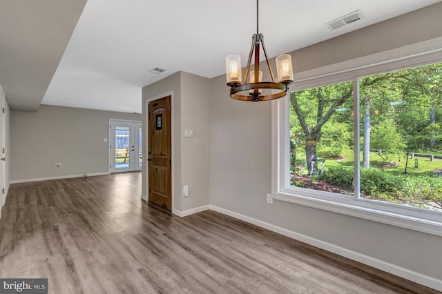  - unfurnished dining area with a chandelier, baseboards, visible vents, and wood finished floors