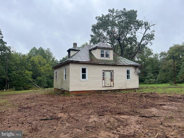 back of house featuring a chimney and metal roof